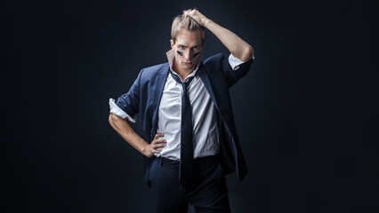 Fototapeta premium In a dimly lit studio, a man in a navy suit adopts a boxing stance, showcasing strength and determination. The sleeves are casually rolled up, enhancing his confident, dynamic pose.
