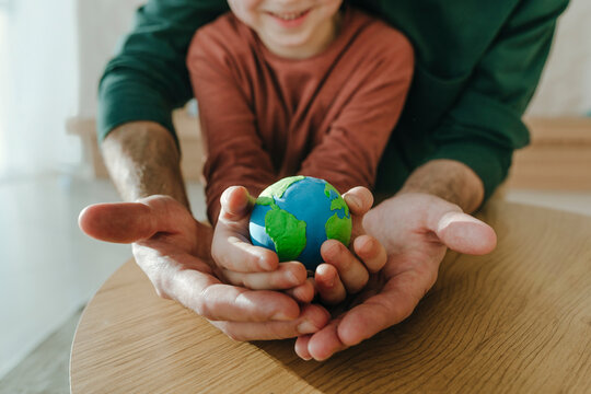 Son and father holding earth globe in hands at home