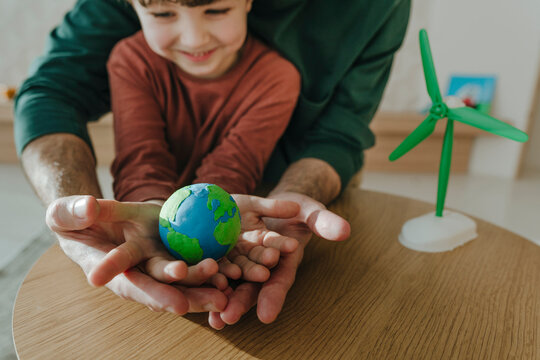 Boy holding earth globe in hands with father at home