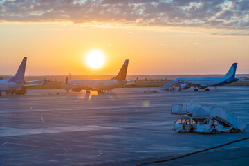 Passenger jets resting on airport tarmac, golden sunrise illuminating wings, capturing serene pre flight aviation moment