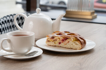 A lush piece of yeast pie with berries in a pastry shop on a table with tea
