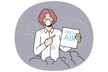 Woman suffers from air pollution and shows paper with inscription fresh air standing in protective mask. Problem of environmental pollution due to coal plants and carbon emissions.