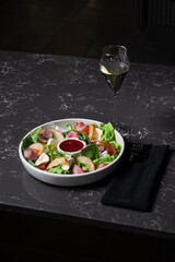 Salad of fresh vegetables and greens with red sauce on a dark table