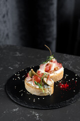Bruschetta two pieces with dried meat and sauce on a black plate