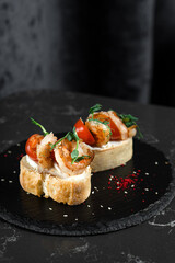 Bruschetta two pieces with shrimps and cherry tomatoes on a black plate