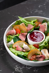 Salad of fresh vegetables and greens with red sauce on a dark table