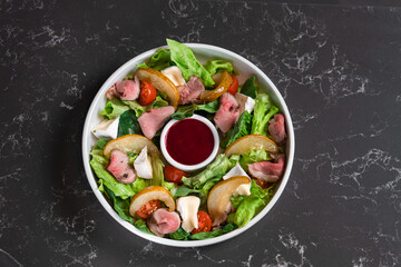 Salad of fresh vegetables and greens with red sauce on a dark table