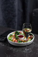 Salad of fresh vegetables and greens with red sauce on a dark table