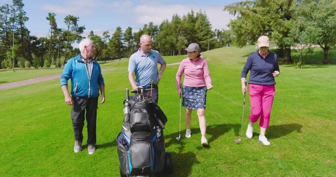 Golf players walking with clubs and talking on golf course