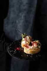 Bruschetta two pieces with dried meat and sauce on a black plate