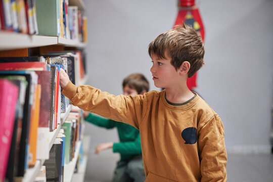Young boy choosing a book from a library shelf. - Powered by Adobe