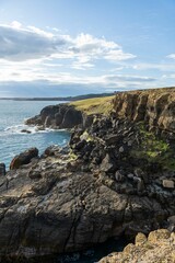 Scenic coastal cliffs with rocky formations under a partly cloudy sky.