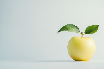 Single yellow apple with green leaves on light background.