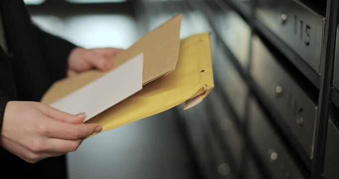Close up woman is opening her mailbox inside a cluster of mailboxes for her apartment. Payment notification letter. Mail shipping concept.