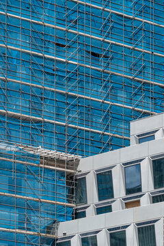 A contemporary building wrapped in scaffolding featuring a striking glass facade that reflects the surrounding environment with geometric precision and modern design elements.