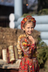 A blonde girl in a national Russian costume on the Maslenitsa holiday. A beautiful russian girl in a national costume made of a fur cape and kokoshnik on the background of a hayloft. 