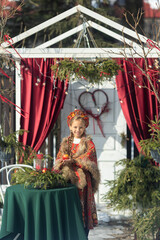 A blonde girl in a national Russian costume on the Maslenitsa holiday. A child in a traditional costume with fur trim and a headdress against a festive backdrop. Winter scene with a beautiful girl