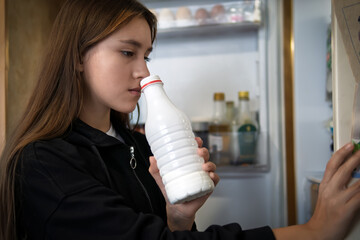 hungry girl open empty refrigerator. A girl sniffs an open bottle of milk. The girl takes out a...