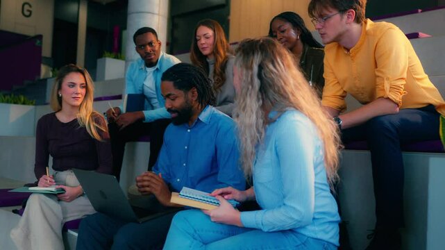 University students engaging in teamwork, utilizing a laptop and notebooks, discussing a project in a modern university hall, captured in a slow motion montage