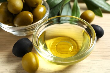 Bowl of fresh olive oil and olives with leaves on the table