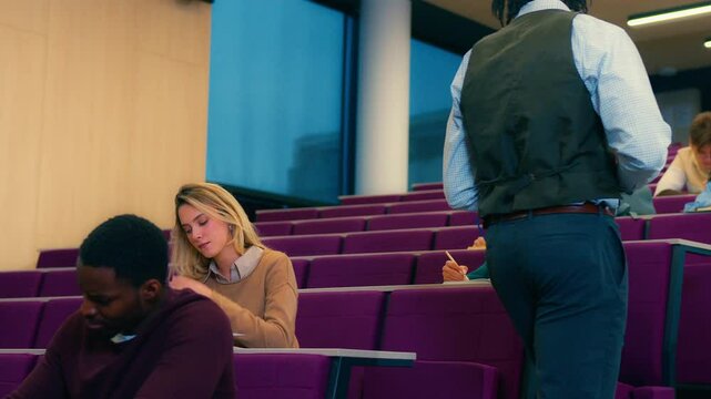 Slow motion sequence showing a university professor assisting a female student during an exam in a lecture hall, providing guidance and support