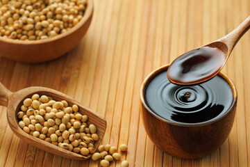 soy sauce pouring in bowl with splash and drop and dry soybeans on wooden table