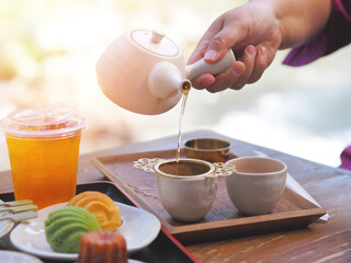 Hand holding teapot pouring hot tea through stainer into a cup