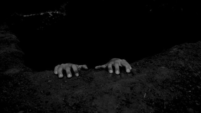The hands of a dead man protrude from the pit. Black and white scary video. Halloween