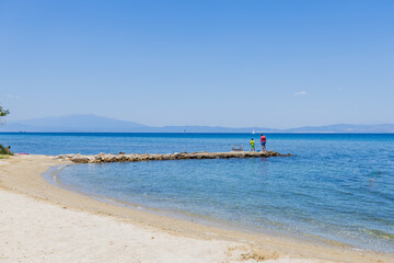 Obraz premium Family enjoying a day at the beach, with a father and child fishing from a small pier.