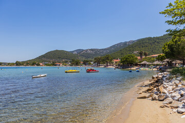 Picturesque coastal scene with crystal-clear turquoise waters, a sandy beach, and a backdrop of lush green hills.