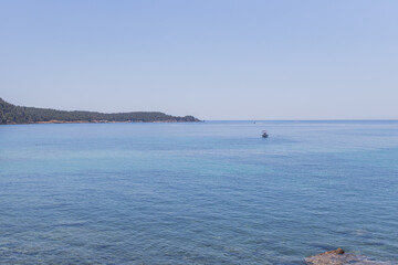 Serene view of the Aegean Sea, with crystal-clear turquoise waters stretching towards the horizon. A small boat sails peacefully.