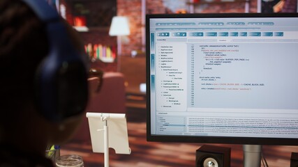 Engineer in home office looking at UI on computer monitor, typing and executing programming code....
