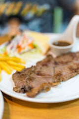 Delicious pork grilled steak served alongside French fries and a small salad on a white plate.