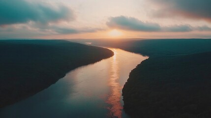 Fototapeta premium Serene sunset over a winding river surrounded by lush green hills and soft clouds in the sky