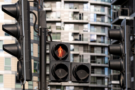 A red pedestrian traffic light stand against a backdrop of modern high-rise buildings, emphasizing the importance of safety in a bustling urban environment.