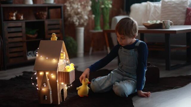 Child, cute boy, playing with toys in a playroom, teddy bear and little ducks with a paper house