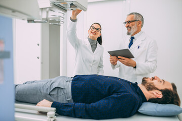 Obraz premium Mature doctor discussing with medical nurse while standing in hospital x ray machine room. Concept of Medicine, Health Care, People.