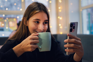 The girl looks at the phone in close-up. Teenage girl with long hair video call on mobile phone on blue background, talking and looking. friendly communication in a cafe.