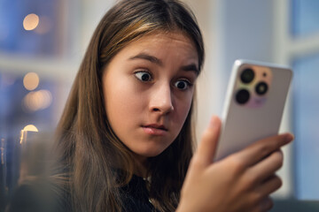 A teenage girl is emotionally talking on the phone in surprise. Shocking news and gossip. Communication video call smartphone. Female face close-up