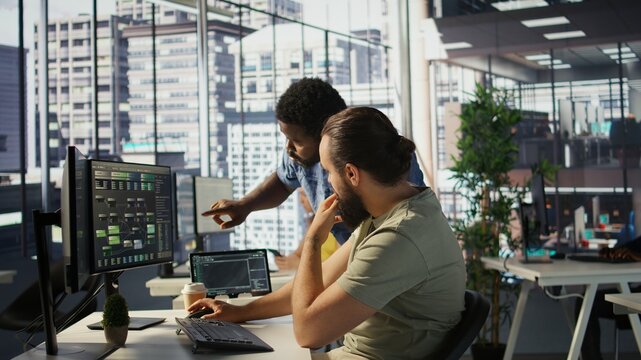 Manager correcting programmer mistakes while conducting code review to fix errors, identifying technical issues with company software. Team leader supervising IT staff member optimizing code, camera B