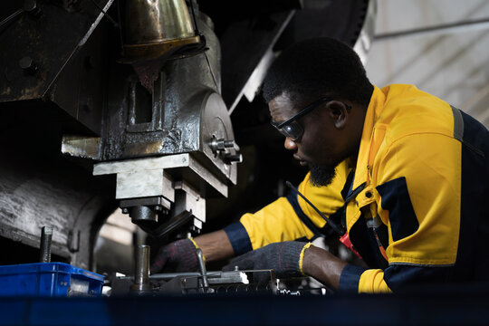 African American male engineer repairing and maintenance heavy lathe machine in industry factory. Male technician worker checking parts of lathe machine at workshop