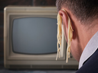 Man in front of TV with noodles on his ears, concept on the topic of deception on television, set...