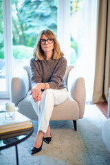 Full length of an attractive blond haired woman relaxing in an armchair in her modern home