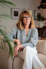 Obraz premium Beautiful woman sitting in an amrchair in her cozy home and smiling at camera