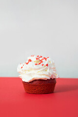 Valentine's greeting card. Red velvet cupcake with hearts shaped sprinkles on red and gray background. Festive tasty dessert for romantic date.