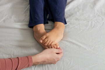 Mother tickling child's feet on bed. Playful bonding moment