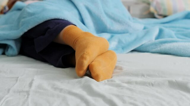 Feet of a child wearing yellow socks, sleeping under a soft blue blanket in bed