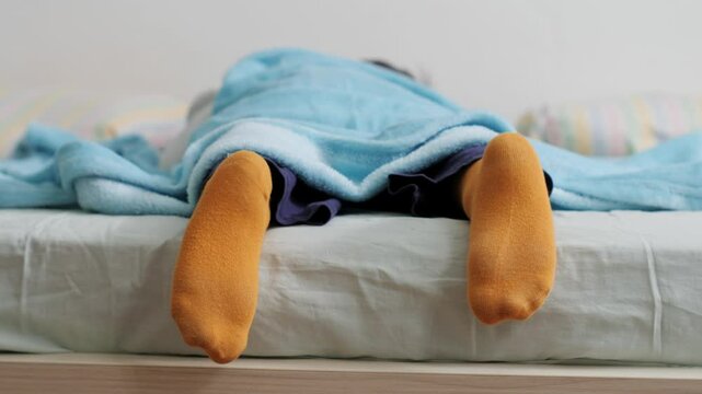 Child sleeping peacefully in bed with yellow socks and blue blanket