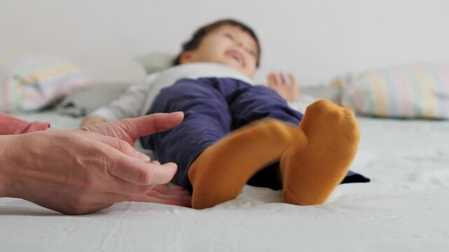 Mother tickling child's feet with yellow socks on bed