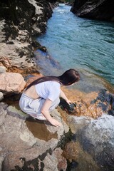 A beautiful young girl is sitting near a river with stormy water. Tourism and outdoor recreation.